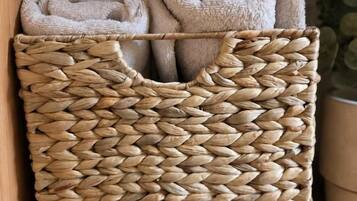 Una cesta tejida con dos toallas enrolladas sobre un estante de madera.