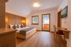 A room with a bed, a desk, and a chair. There is a window and a door leading outside. - Alpenchalet Vital (Neustift im Stubaital)