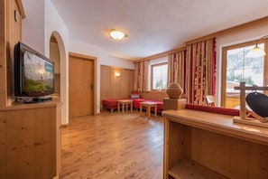 A wooden interior with a television, a sofa, a table, and a window with curtains. - Alpenchalet Vital (Neustift im Stubaital)