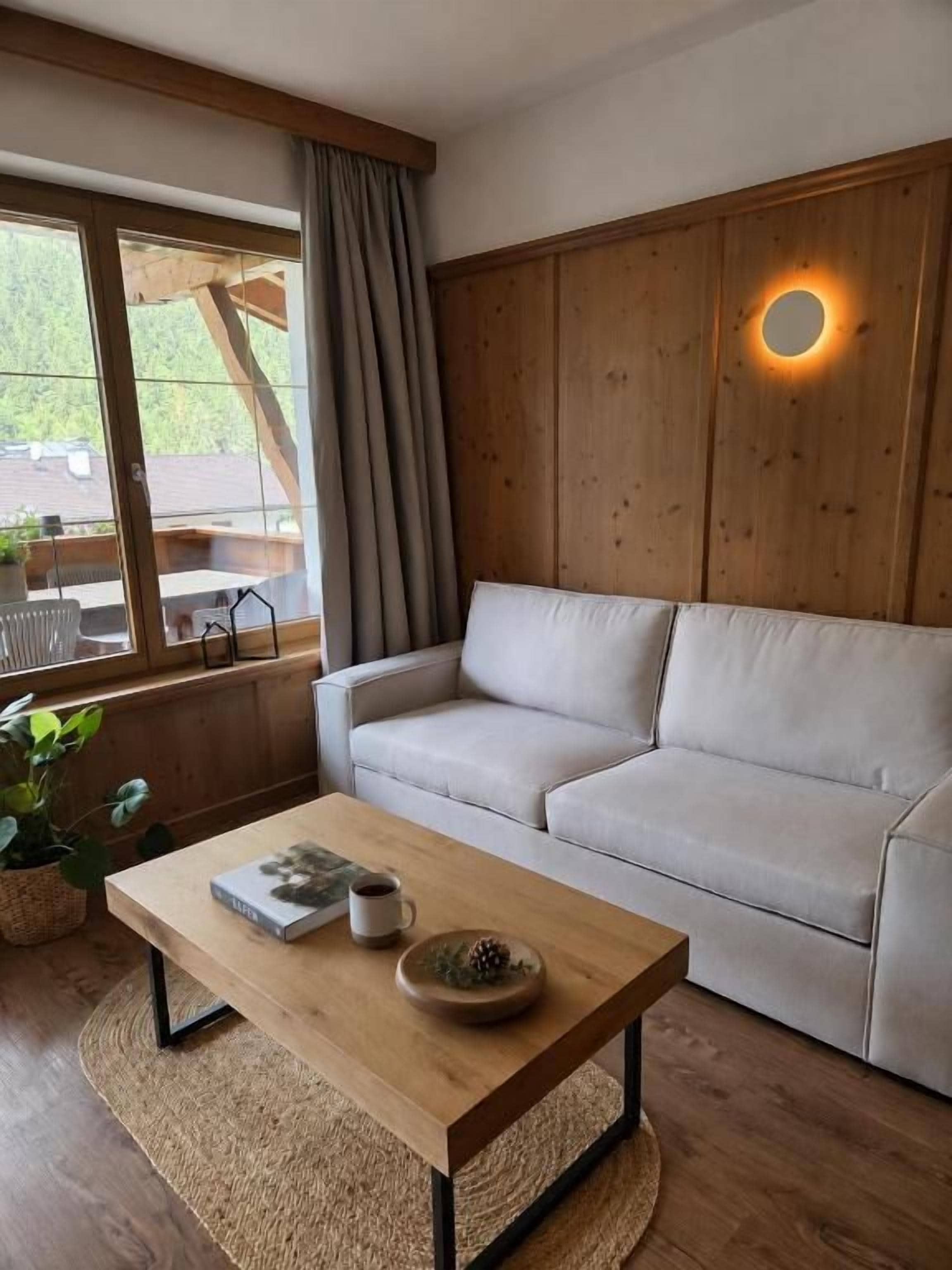 Une pièce comprenant un canapé, une table basse, une fenêtre avec des rideaux et un mur en bois agrémenté d’un luminaire.