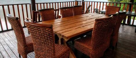 Terraza de madera con mesa y sillas, con vista a un cuerpo de agua y vegetación.