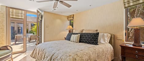 A bedroom with a bed, a ceiling fan, a nightstand, a lamp, and a view of the outdoors.