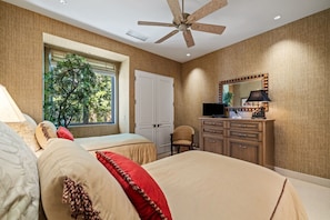 A bedroom with a bed, a chair, a desk with a lamp, a television, and a window with a view of trees. - The Reserve - Luxury 4-Bedroom Retreat Plus Office in Peaceful Indian Wells (Indian Wells)