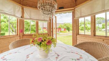 Een kamer met houten vloeren, een ronde tafel, een kroonluchter en uitzicht op een tuin.
