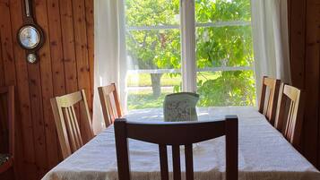 A wooden interior with a dining table, chairs, a clock, and a window with curtains.