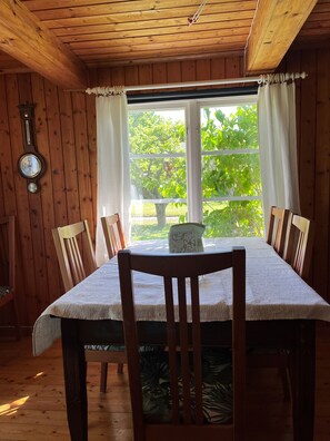 Un interior de madera con una mesa de comedor, sillas, un reloj y una ventana con cortinas.