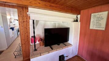 Een kamer met een open haard, een televisie en een keuken in de achtergrond.
