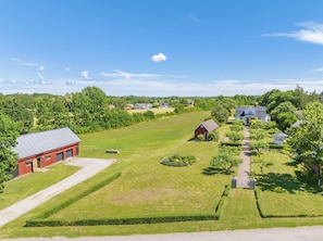 A rural landscape with a large open field, a red barn, and a blue house with a garden.