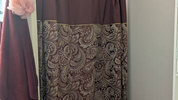A bathroom with a shower curtain featuring a paisley pattern, a towel rack with a pink towel, and a white shelf with a white towel.