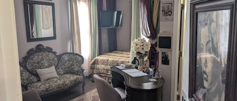 A bedroom with a bed, a desk with a chair, a sofa, and a mirror.
