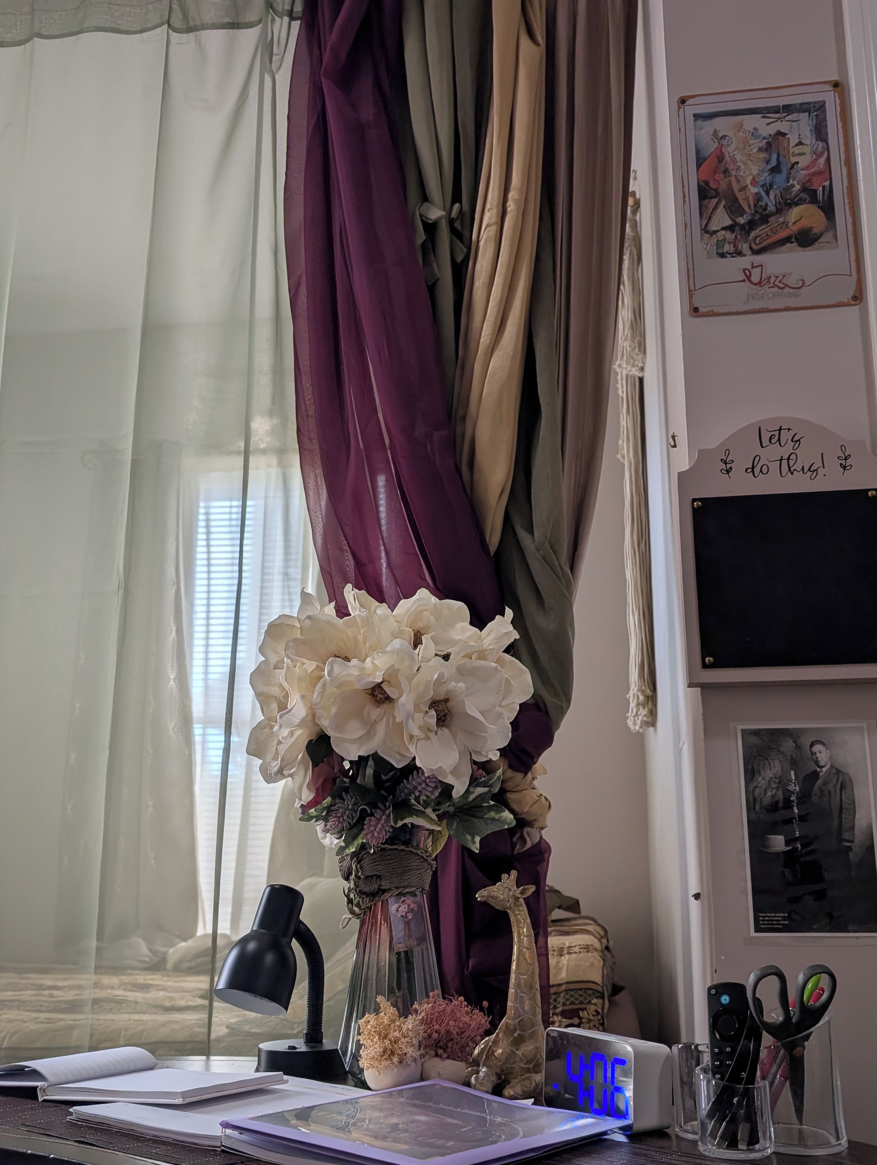 A desk with a lamp, a vase with flowers, a clock, and various office supplies.