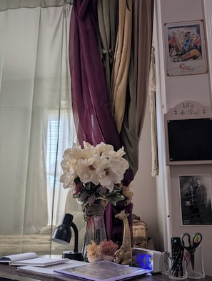 Una scrivania con una lampada, un vaso di fiori, una sveglia e diversi articoli di cancelleria.