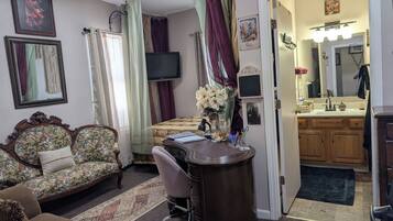 A room with a bed, a desk, a chair, a television, and a bathroom visible through an open door.
