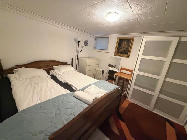 A bedroom with a double bed, a bedside table, a chair, a radiator, a mirror, and a wardrobe.