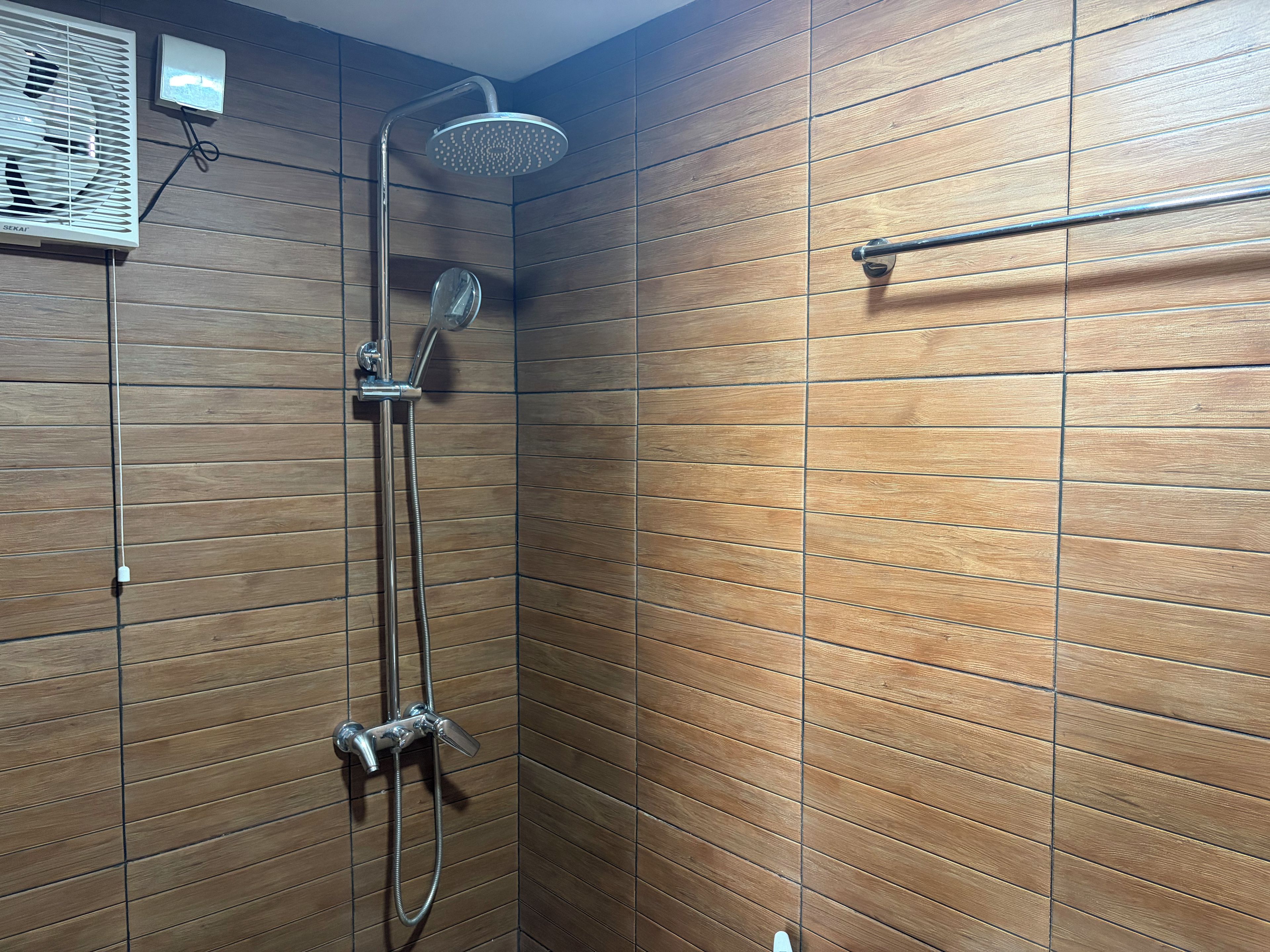 A shower with a handheld showerhead and a wall-mounted control panel.