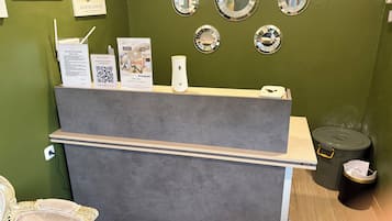 A reception desk with a grey counter, a white chair, and a small trash bin.