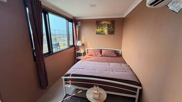 Habitación de hotel con cama, mesita de noche, lámpara, un cuadro y vistas al exterior.