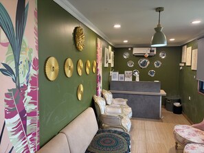 Un área de recepción con pared verde, un mostrador, un sofá, un tapete estampado y placas decorativas en la pared.