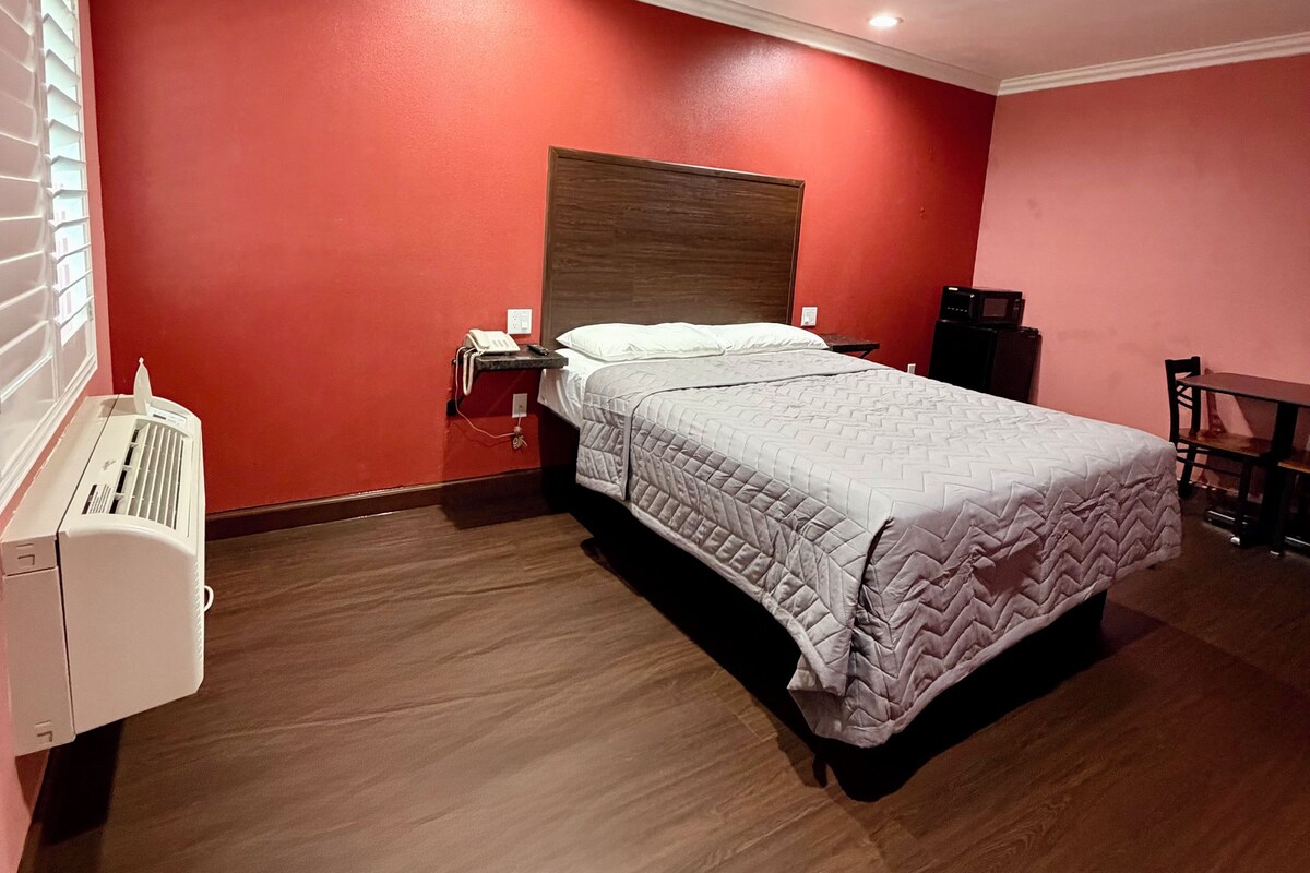 A bedroom with a bed, a bedside table, a heater, and a window with blinds.