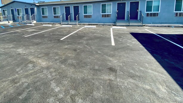 A motel with a row of rooms, each with a door number and a window. There are parking spaces in front of the building. - HOLLYWOOD MOTEL (Los Angeles)