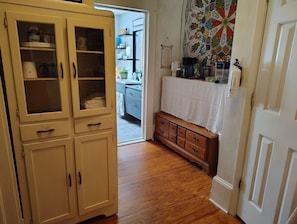 A hallway with a wooden cabinet, a small wooden dresser, and a kitchen area in the background.