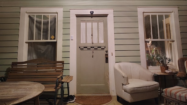 Una habitación con un banco de madera, un sillón blanco, una mesita y una puerta con ventanal.