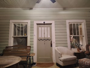 A room with a wooden bench, a white armchair, a small table, and a door with a window.