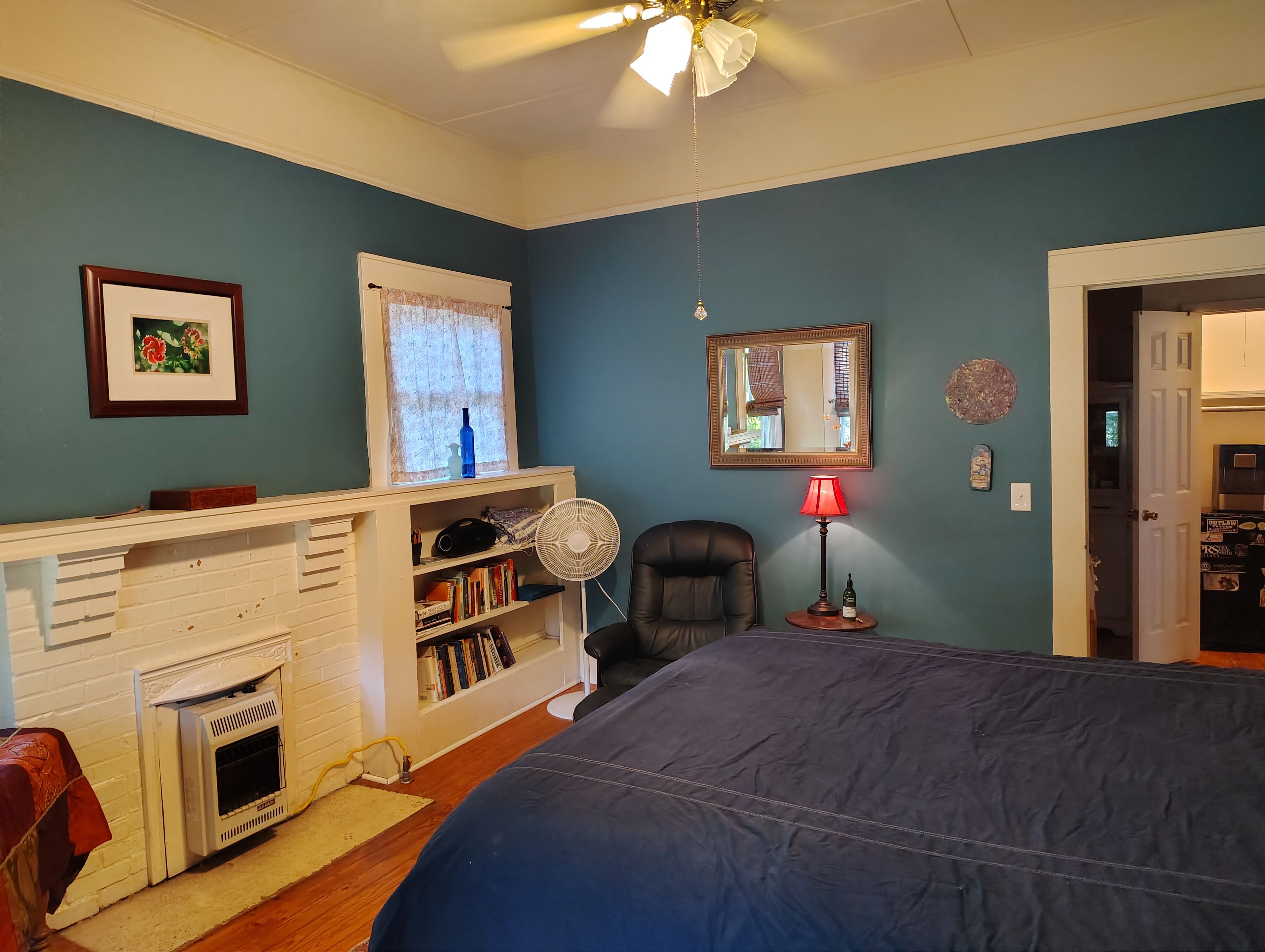 A bedroom with a bed, a fireplace, a bookshelf, a desk, and a window with curtains.