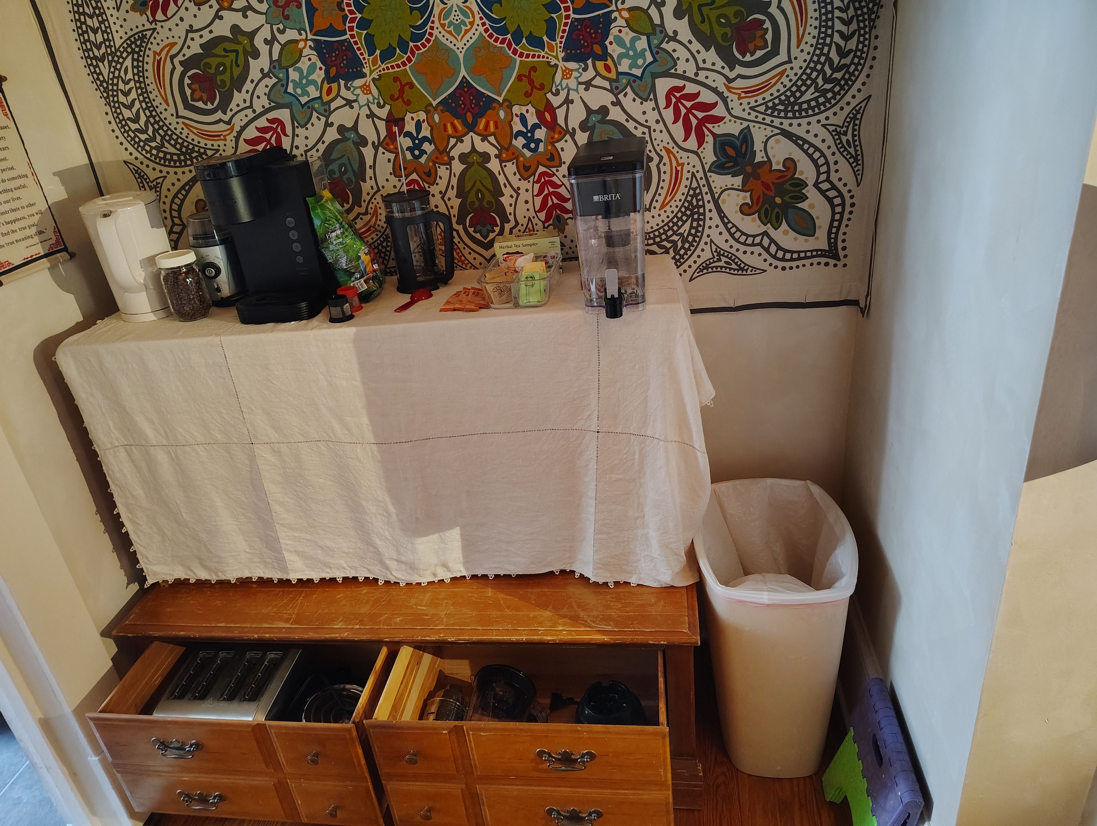 A small kitchenette area with a coffee maker, tea maker, and various kitchen items on a table.