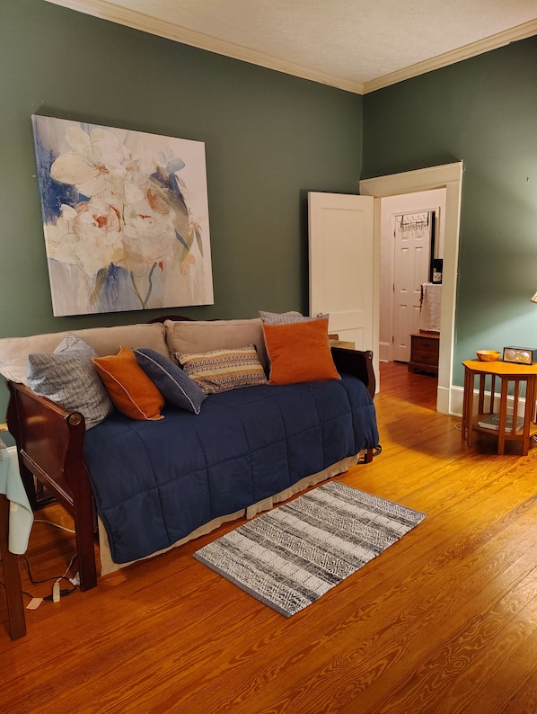 A living room with a blue sofa, patterned cushions, a rug, and a painting on the wall.