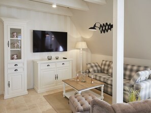 A living room with a flat-screen TV, a white cabinet, a plaid sofa, a coffee table, and a lamp. - Holiday Apartment in Busum With Swimming Pool (Büsum)