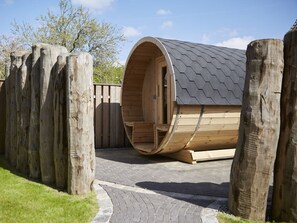 A wooden sauna structure with a sloped roof, surrounded by wooden posts and a paved entrance. - Holiday Apartment in Busum With Swimming Pool (Büsum)