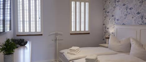 Un dormitorio con cama, mesitas de noche, lámpara y ventana con persianas.