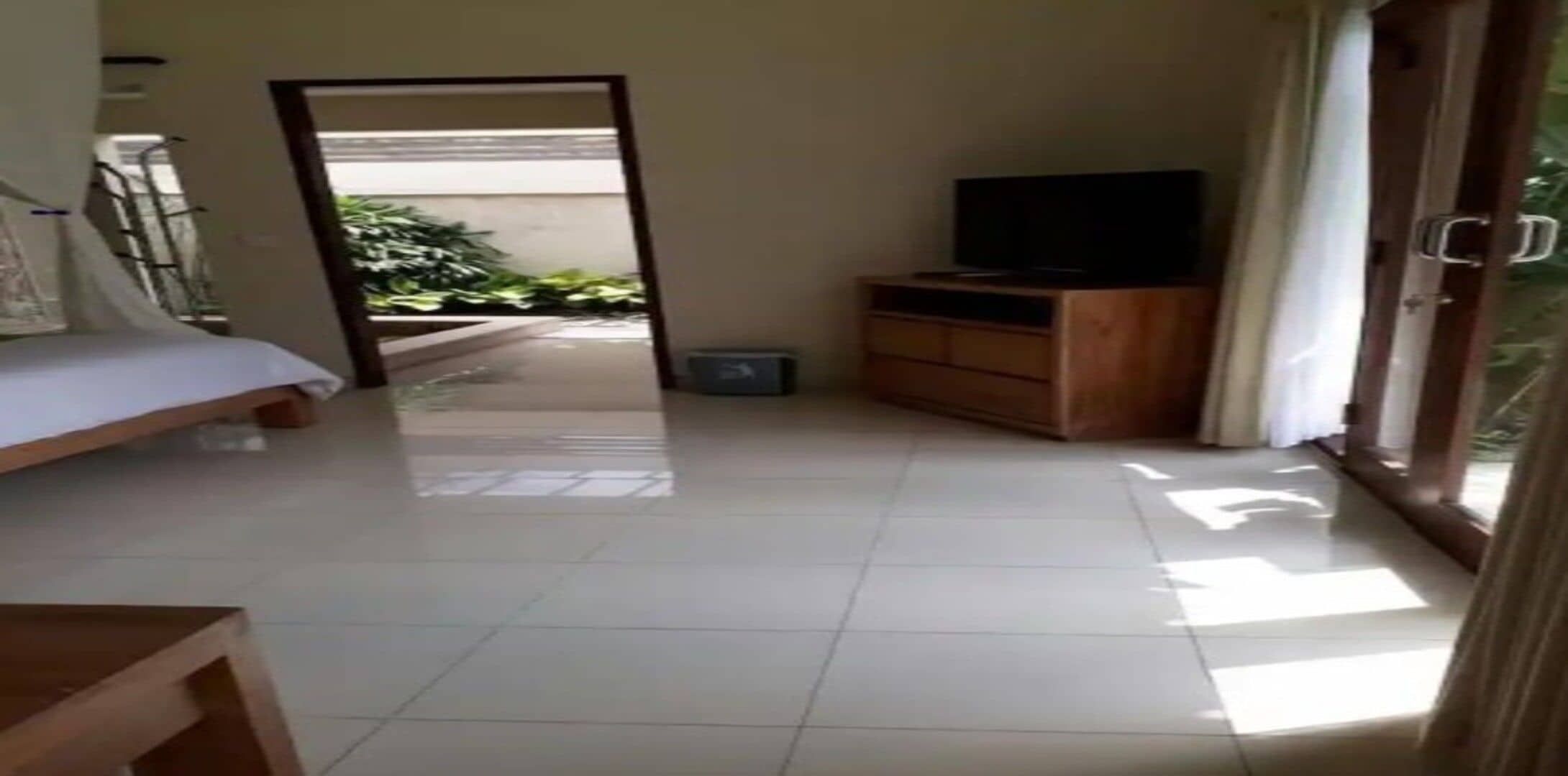 Ein Hotelzimmer mit einem Bett, einem Fernseher auf einer Holzkommode und einer Glastür, die zu einem Balkon führt.
