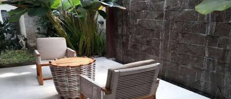 A patio area with a stone wall, two wicker chairs, a round wooden table, and a potted plant.