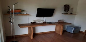 Una habitación con un escritorio de madera, un televisor de pantalla plana montado en la pared, un refrigerador pequeño y un acuario sobre una estantería.