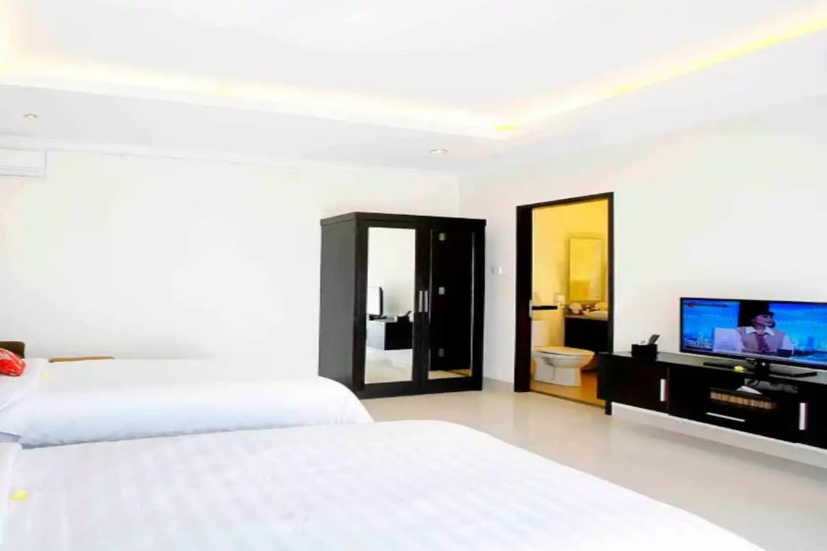A modern hotel room with two beds, a television, and a bathroom.