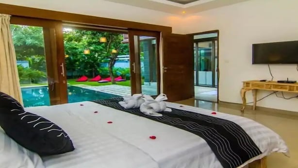 Habitación de hotel con cama, escritorio, televisión y vistas a una piscina y follaje.