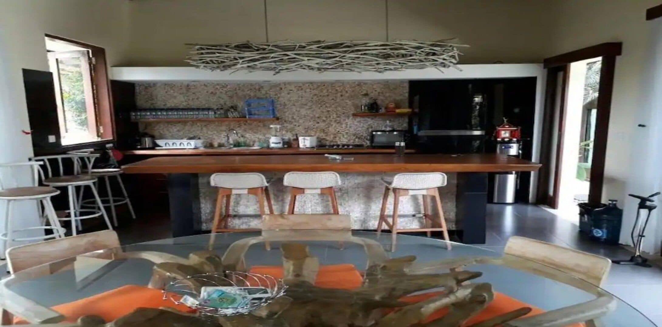 A modern kitchen with a central island, bar stools, and a dining table with orange cushions.
