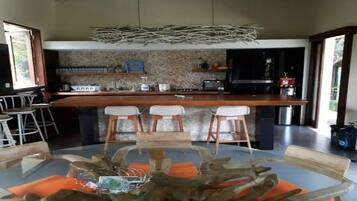 A modern kitchen with a central island, bar stools, and a dining table with orange cushions.