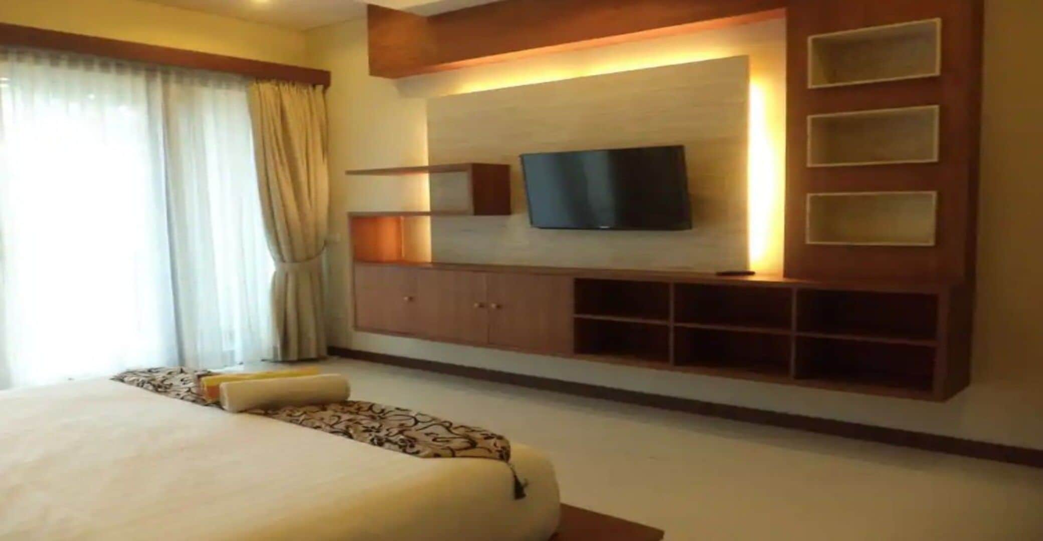 Habitación de hotel con una cama grande, un televisor de pantalla plana montado en la pared y un mueble empotrado para entretenimiento.