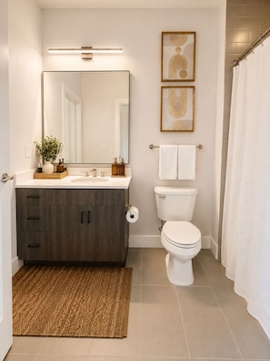 A modern bathroom with a dark wood vanity, a white toilet, and a shower curtain. - The Ivory Suite Midown (Atlanta)