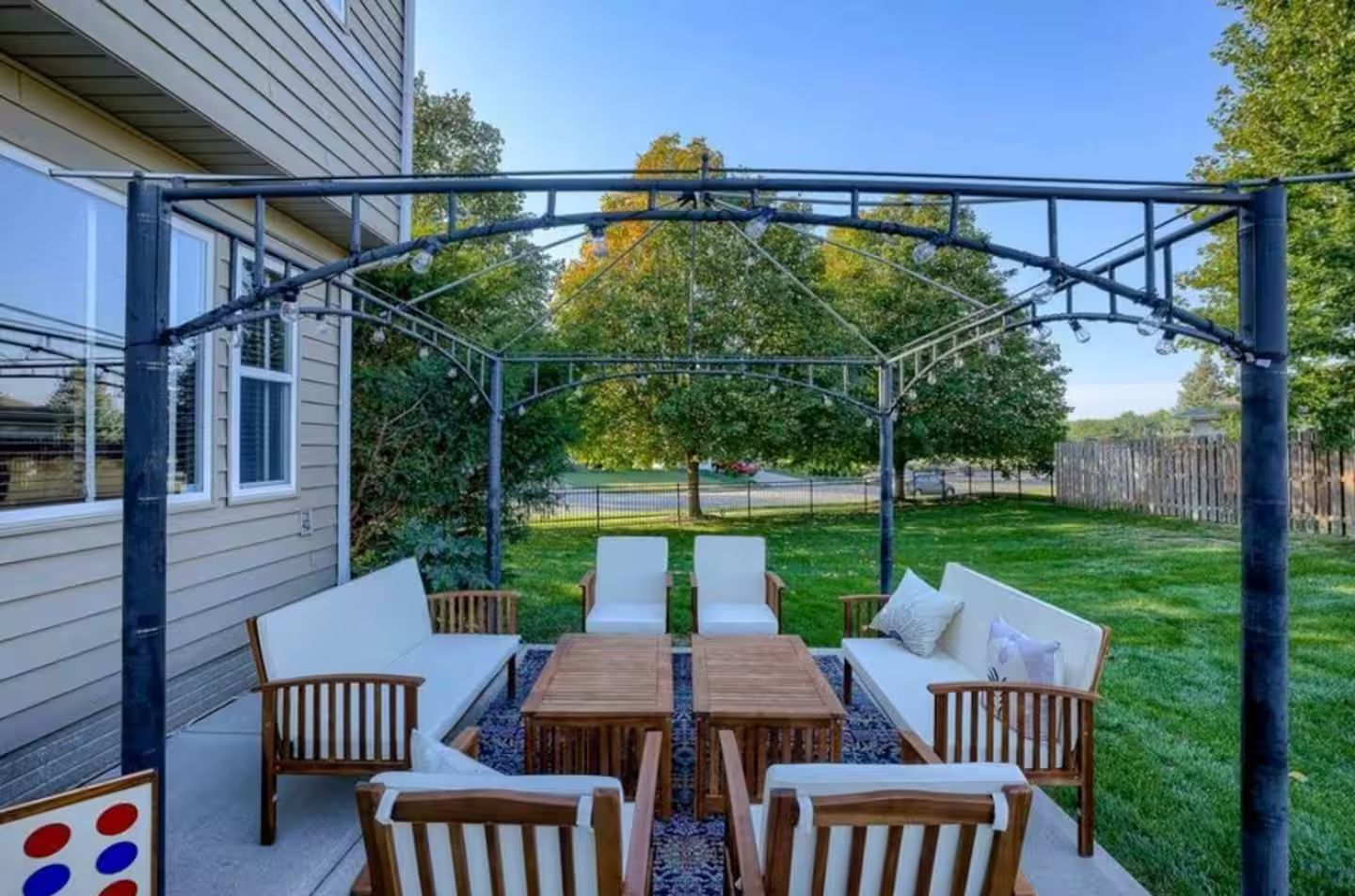 An outdoor patio with a pergola, seating area, and a view of a residential street.