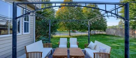 An outdoor patio with a pergola, seating area, and a view of a residential street.
