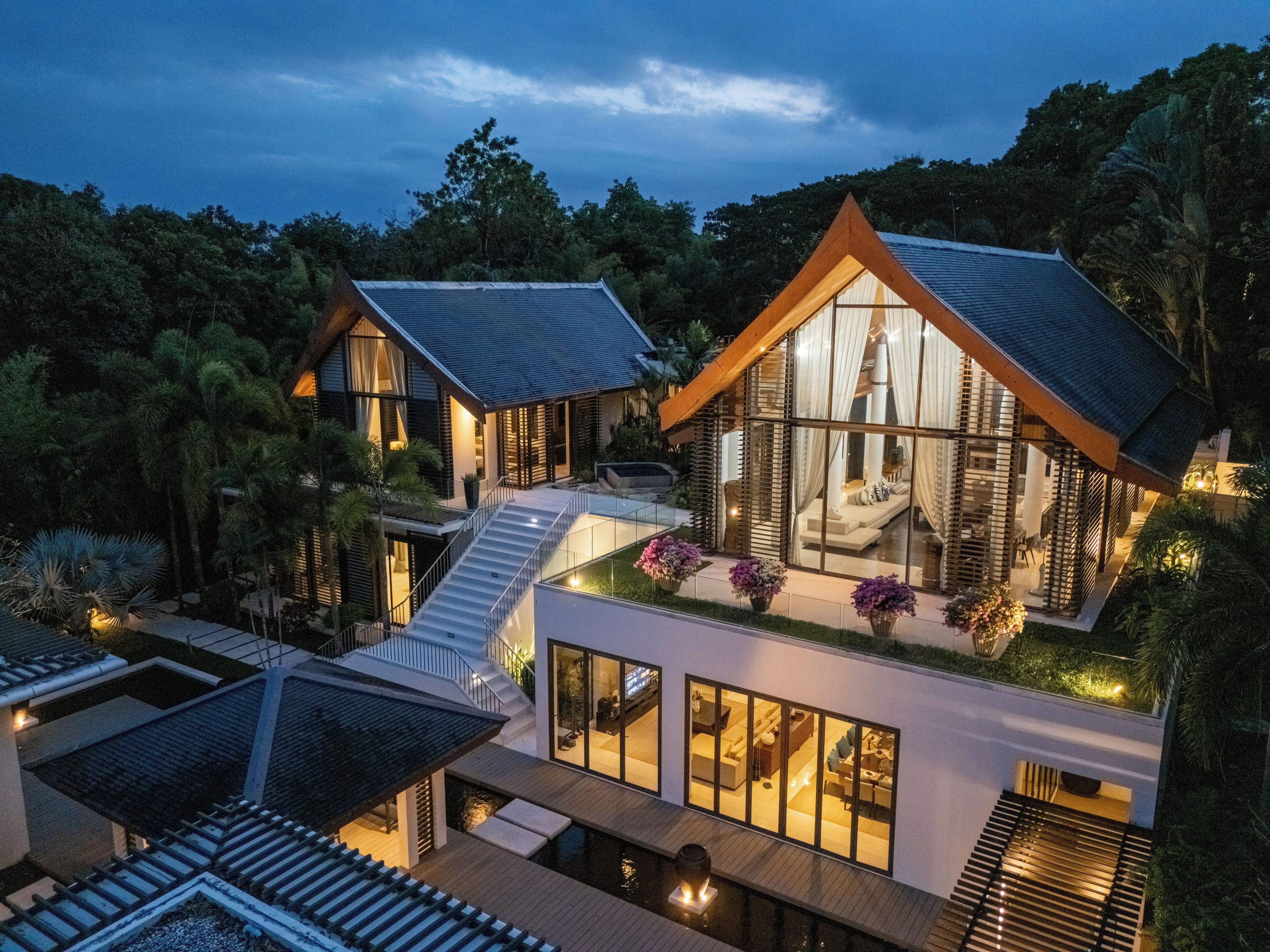 Una casa moderna de dos pisos con fachada de vidrio, terraza de madera y una pequeña piscina.