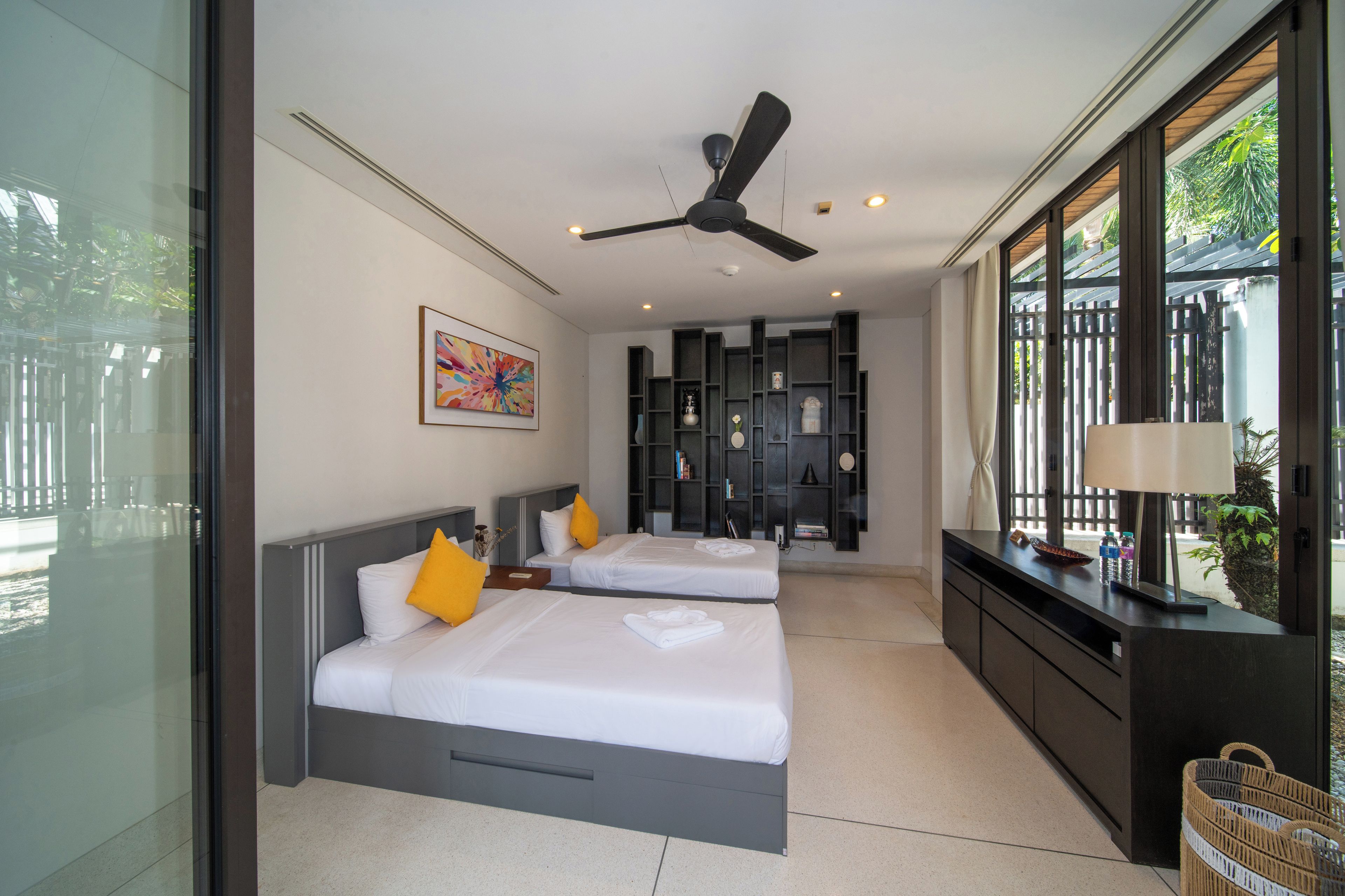 Habitación de hotel con dos camas, un ventilador de techo, un ventanal grande y vistas a zonas verdes.