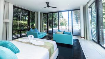 Una habitación de hotel moderna con una cama grande, dos sofás, un ventilador de techo y ventanas amplias con persianas.