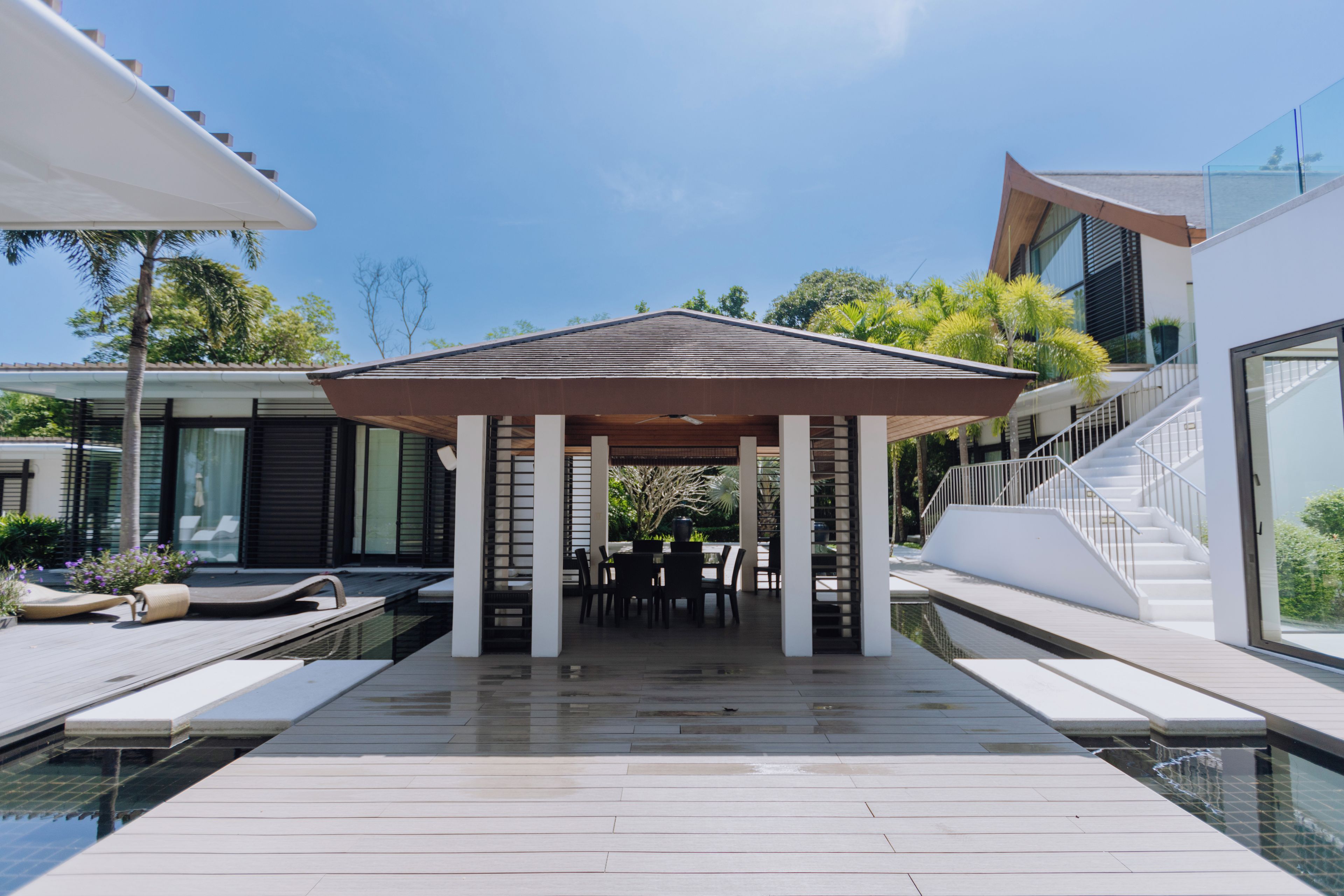 A covered outdoor area with a pool, seating, and a staircase leading to a building.