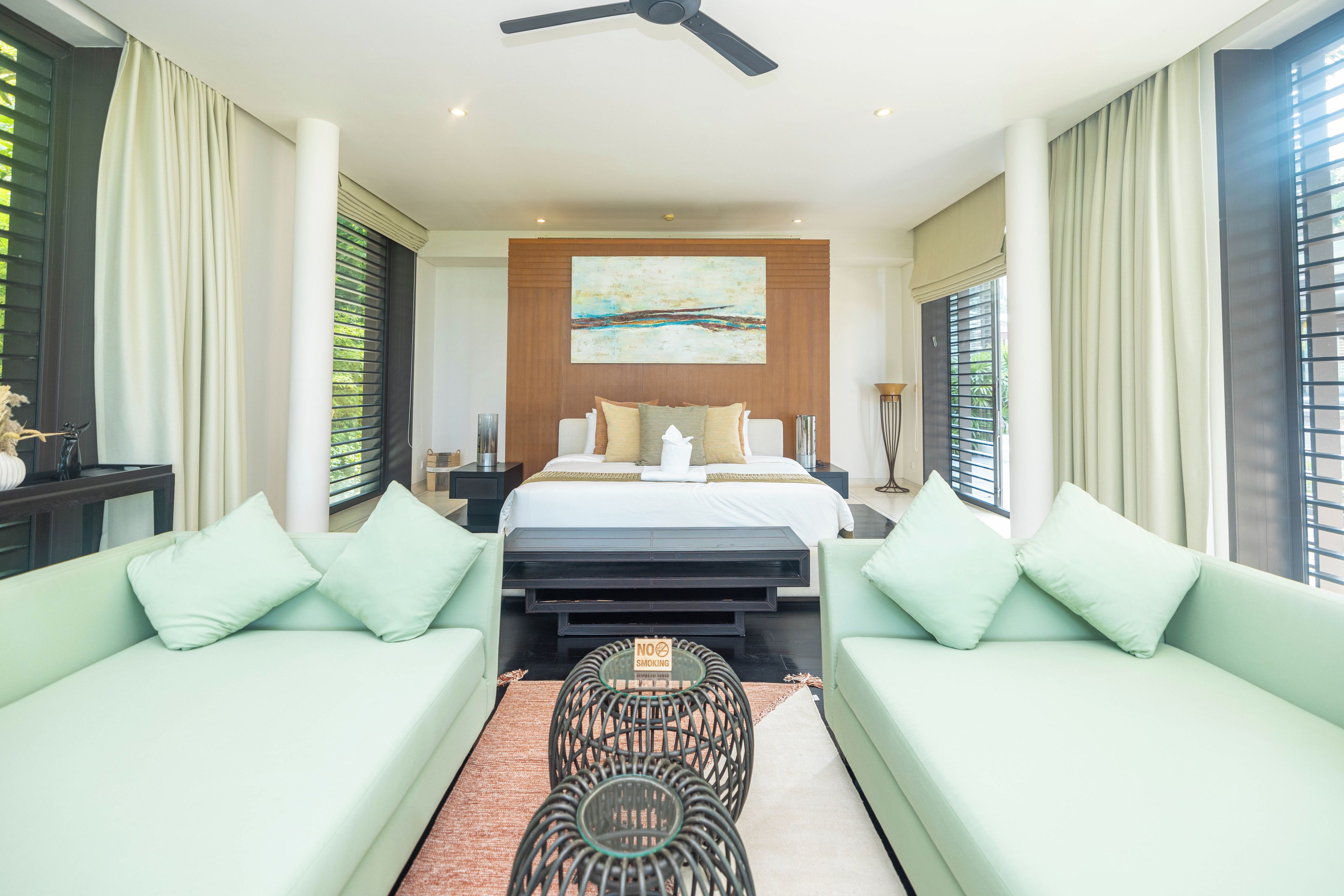 A modern bedroom with a bed, two sofas, a coffee table, and a ceiling fan.