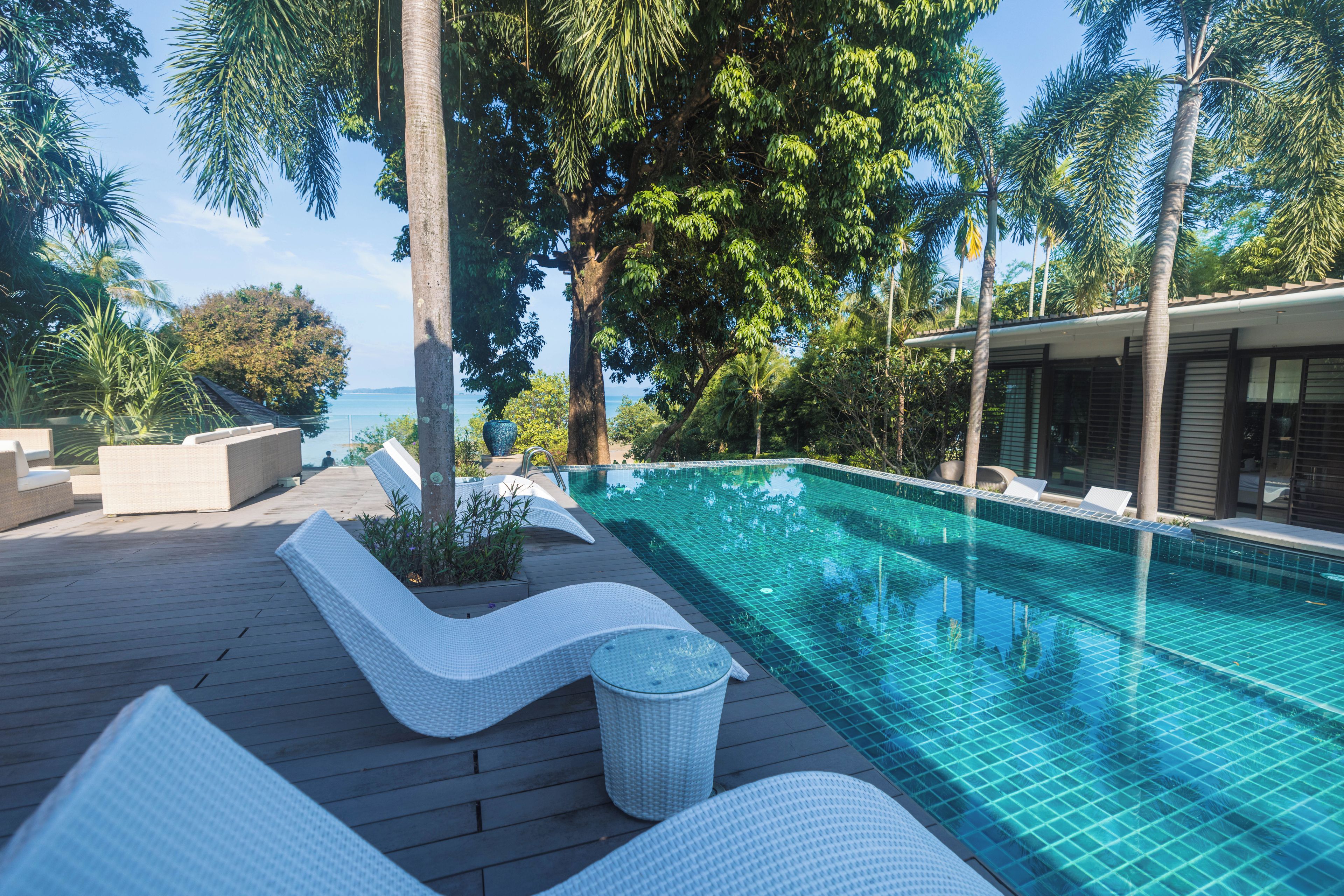 Una piscina con agua azul cristalina, rodeada de una terraza de madera y sillones de descanso.